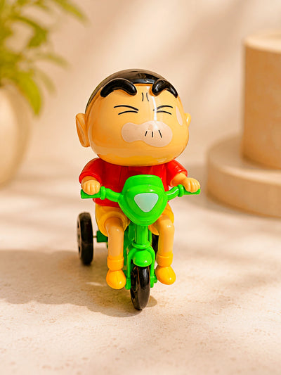 A small plastic toy figurine of a cartoon boy riding a green tricycle, set against a warm beige background with soft-focus decorative props.