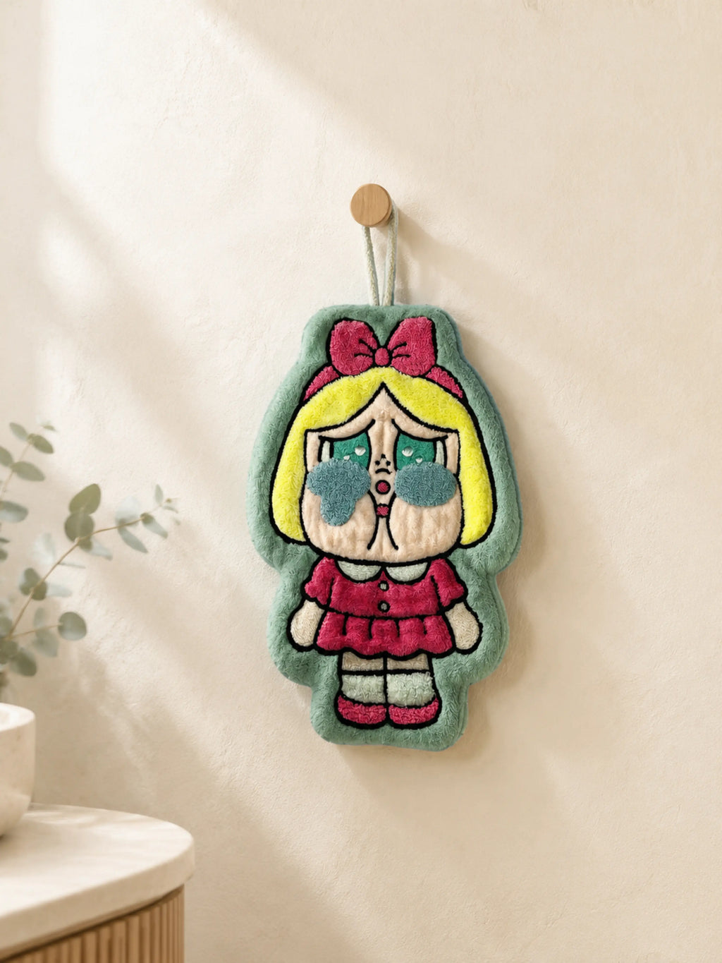 Cute mint green character hand towel hanging from a wooden wall peg in a warm minimalist bathroom