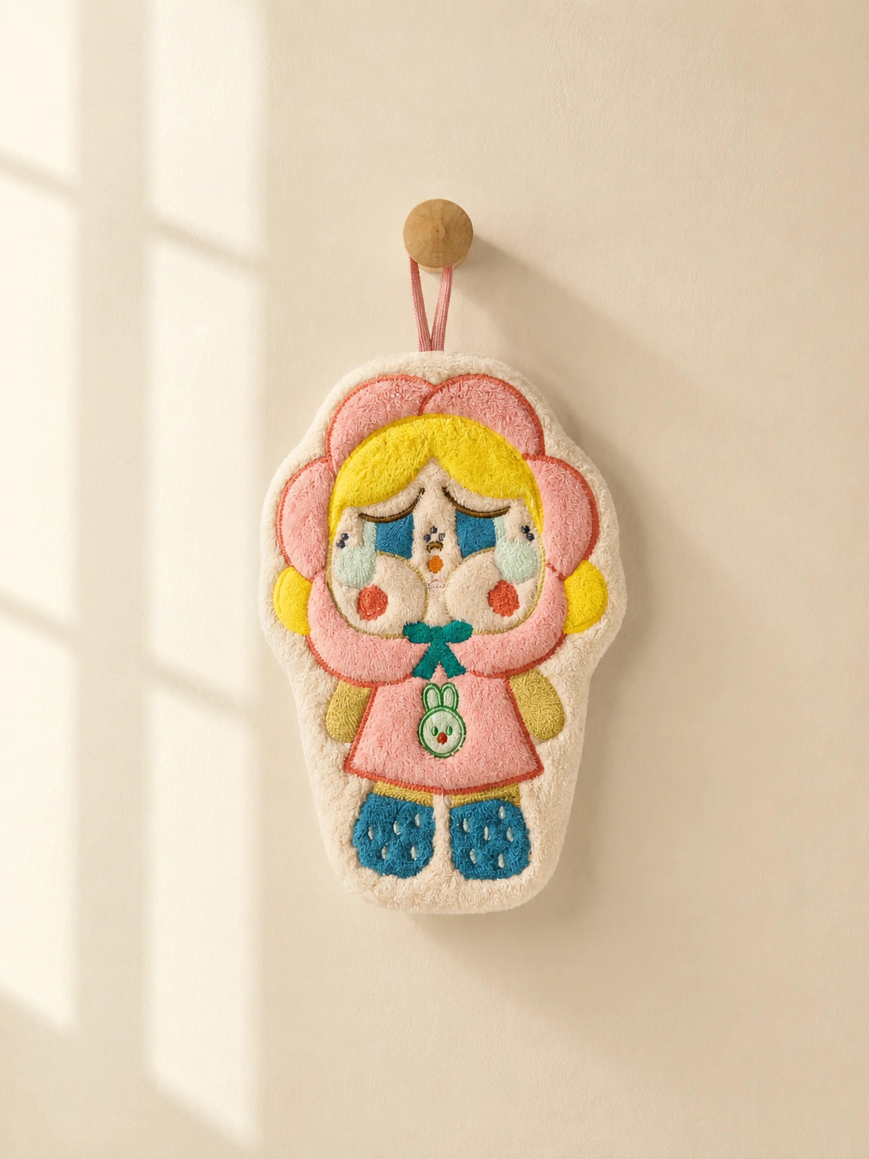 Cute pink flower hood character hand towel hanging from a wooden wall peg in a warm minimalist bathroom