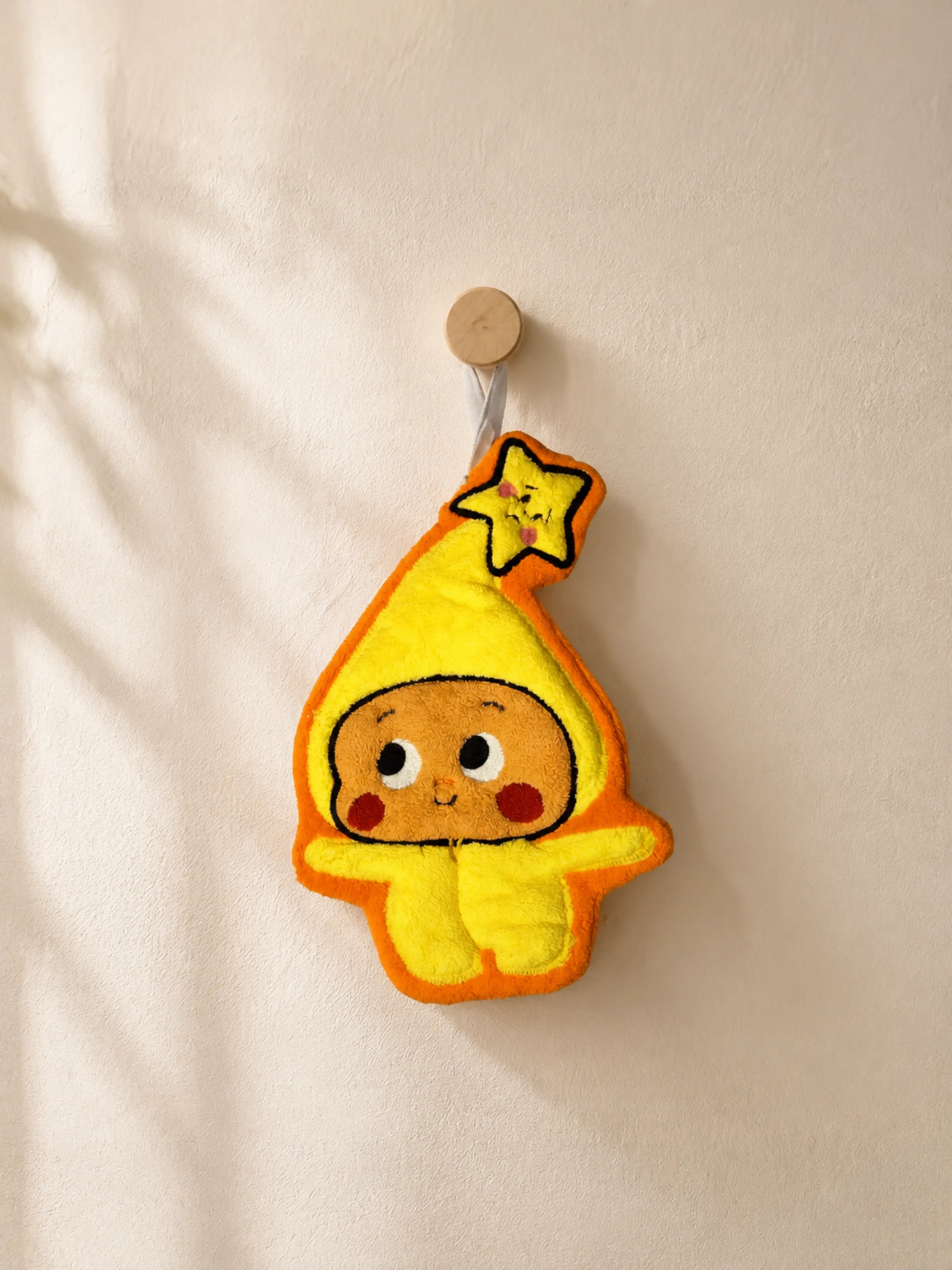 Cute orange and yellow star hood hand towel hanging from a wooden wall peg in a warm minimalist bathroom