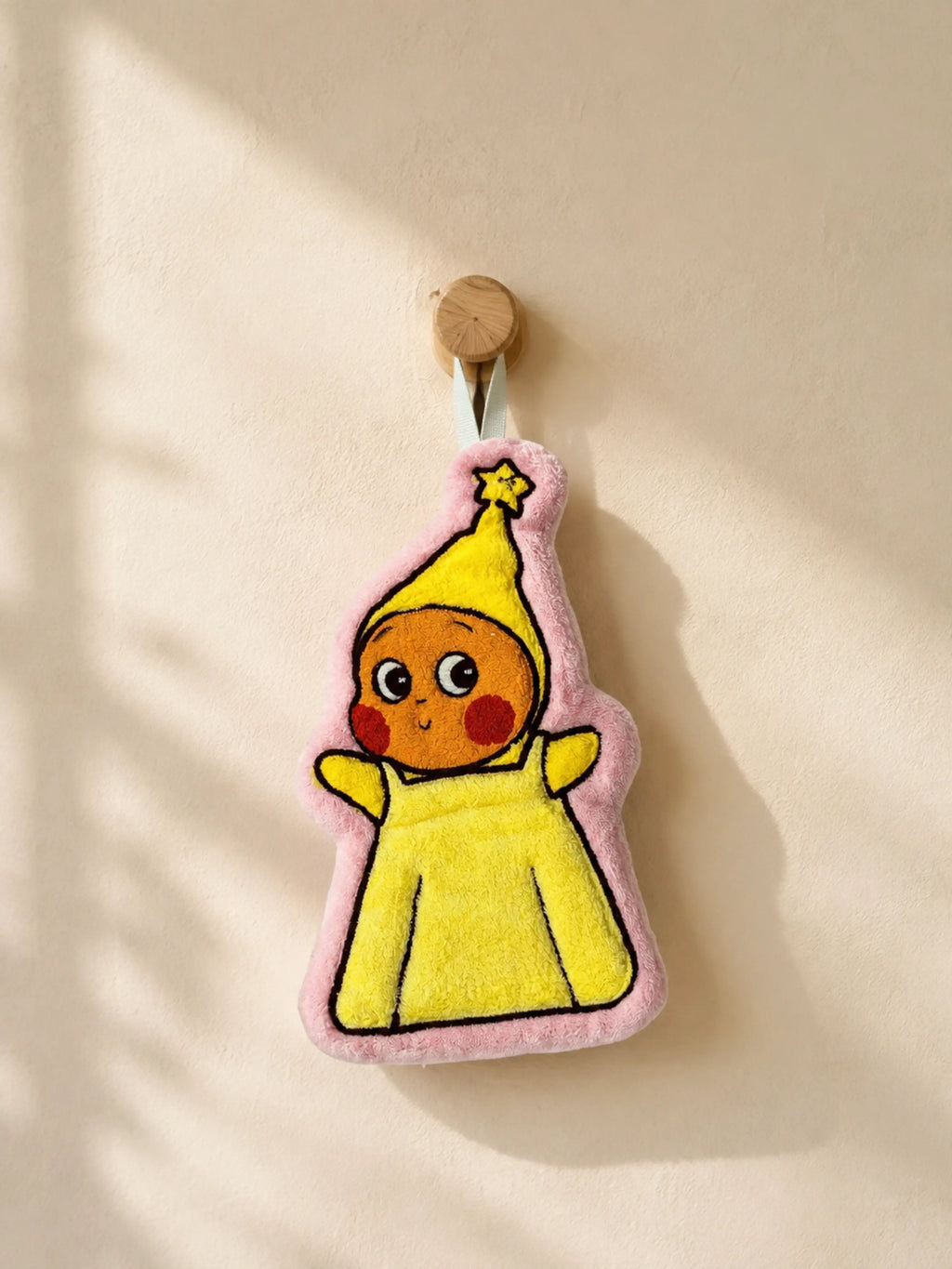 Cute pink bordered character in a yellow outfit hand towel hanging from a wooden wall peg in a warm minimalist bathroom