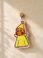 Cute pink bordered character in a yellow outfit hand towel hanging from a wooden wall peg in a warm minimalist bathroom