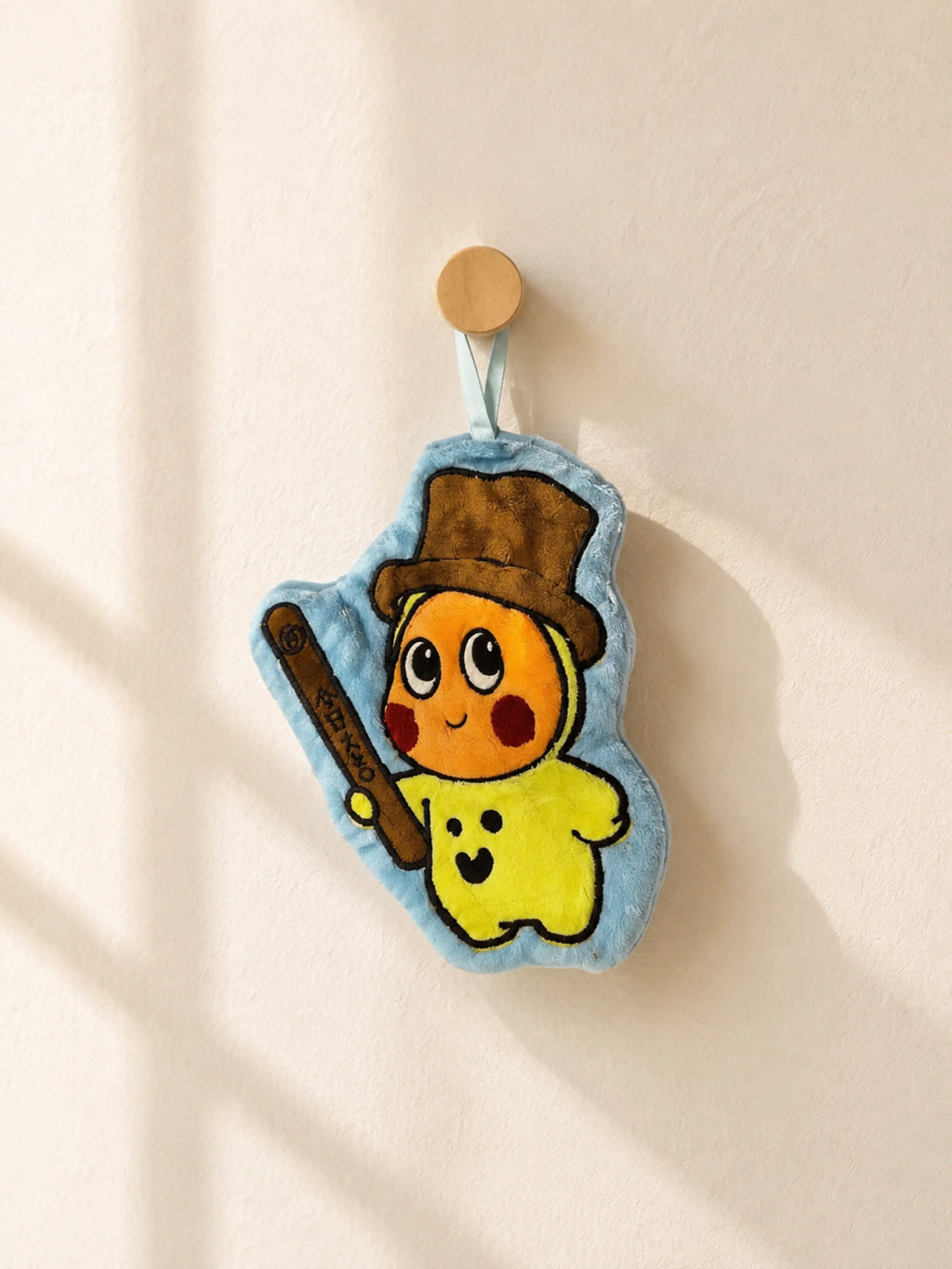 Cute blue bordered top hat character hand towel hanging from a wooden wall peg in a warm minimalist bathroom