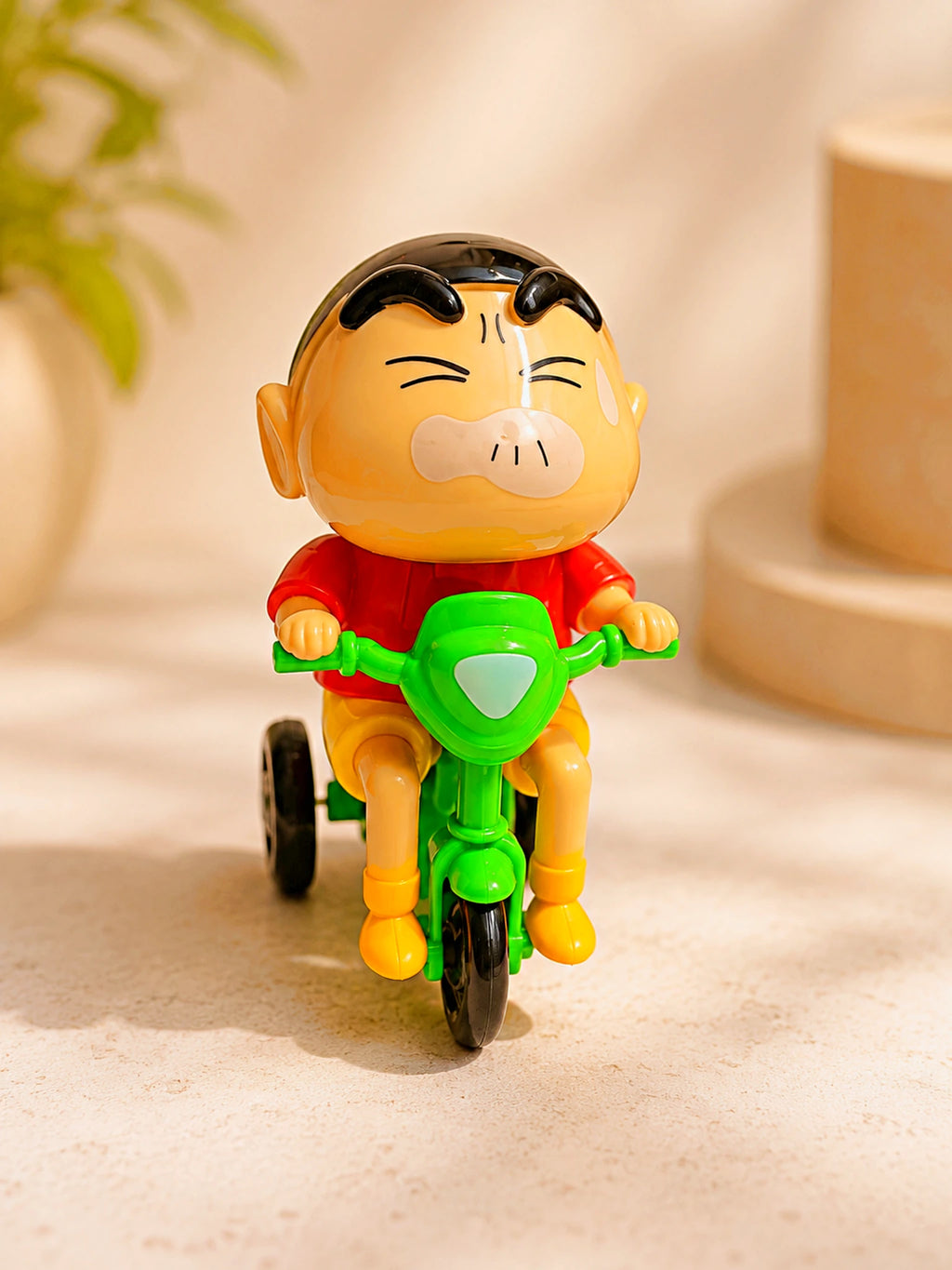A small plastic toy figurine of a cartoon boy riding a green tricycle, set against a warm beige background with soft-focus decorative props.